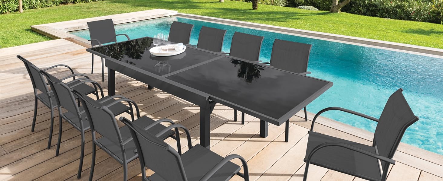avec table rectangulaire foncée et huit chaises assorties à côté d'une piscine. Une terrasse en bois entoure la piscine, avec une végétation luxuriante et des palmiers en arrière-plan.