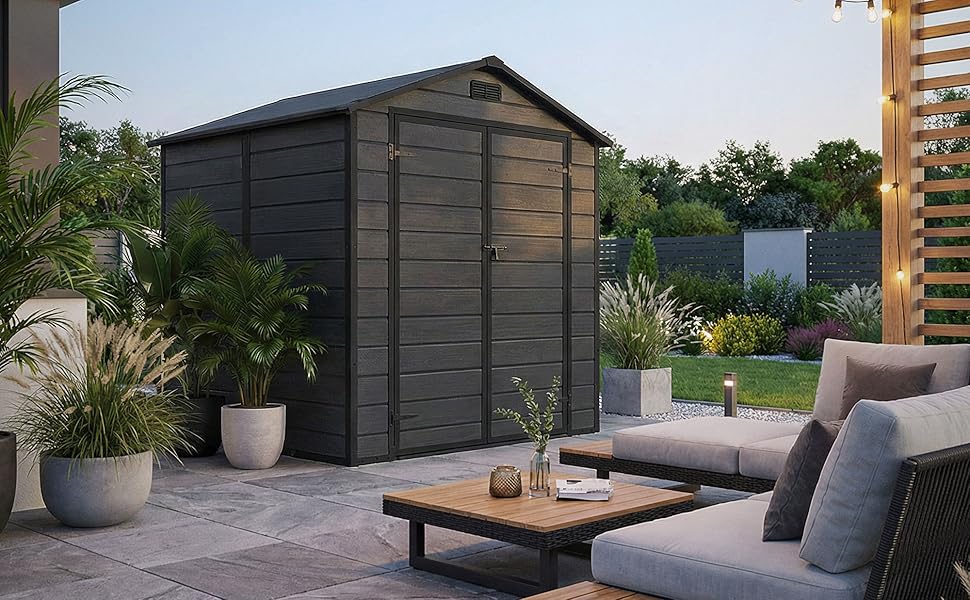 Aménagement de patio extérieur moderne comprenant un cabanon ou une armoire de rangement gris foncé, avec un mobilier d'extérieur contemporain, y compris un canapé gris et une table basse en bois, entouré de plantes en pot.
