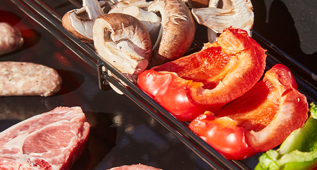 Assortiment de matières premières disposées dans un réglage de cuisson. Poivrons rouges frais, légumes-feuilles et morceaux de viande crue présentés en portions séparées sur une surface foncée.