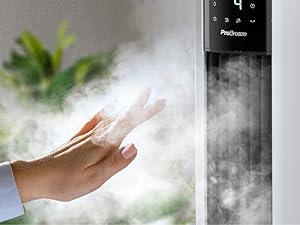 Main tendue vers la brume d'un humidificateur à tour noire. Plante verte visible en arrière-plan.