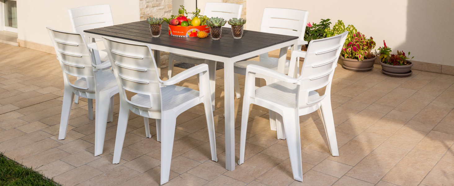 Salle à manger sur la terrasse extérieure avec un ensemble de meubles blancs, y compris des chaises et des tables, sur une surface en béton avec des éléments décoratifs.