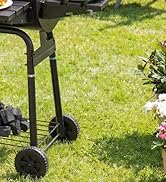 Scène extérieure montrant un pied ou une roulette de meuble à roues noires sur de l'herbe verte près des plantes du jardin et de la structure du patio. Gros plan de la fixation de la roue dans un environnement naturel.