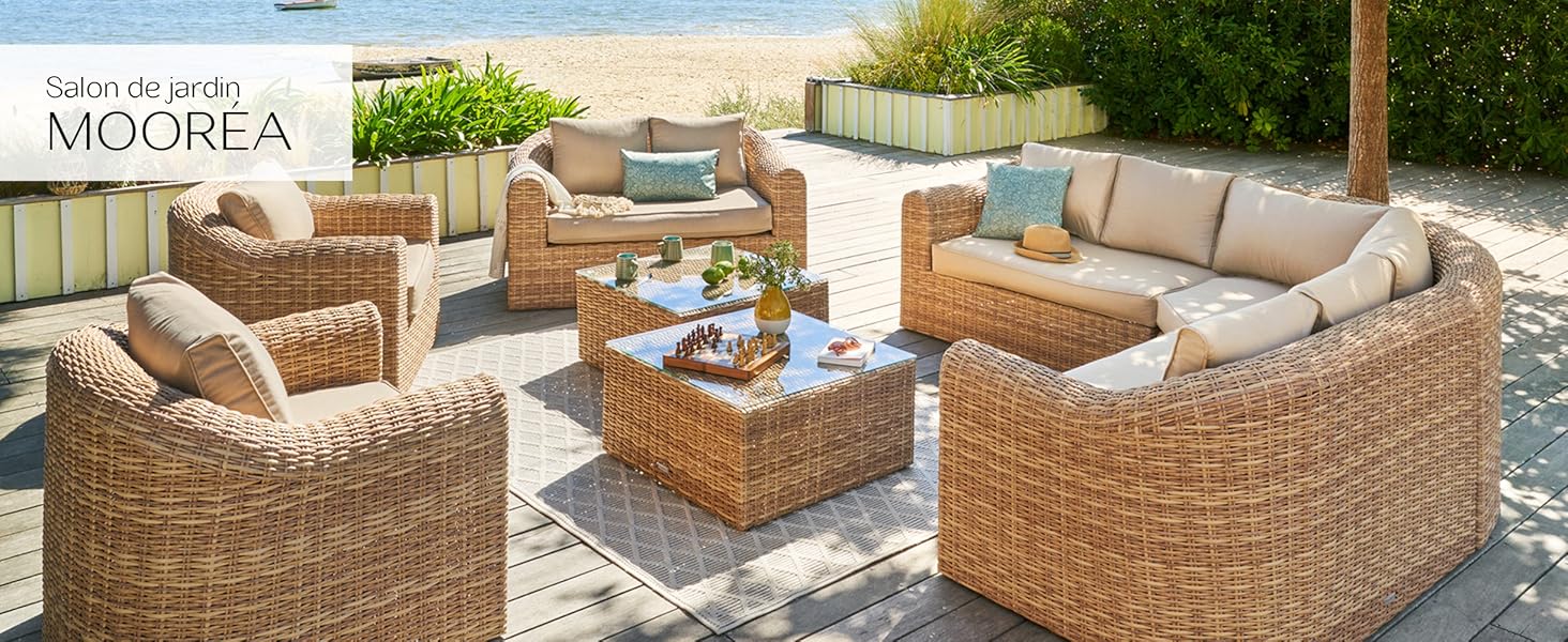 comprenant des canapés, des fauteuils et une table basse en rotin tressé. Coussins beiges sur les sièges. Disposé sur une terrasse de couleur claire avec des jardinières en arrière-plan