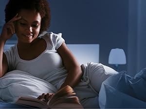 Personne au lit la nuit utilisant un smartphone, éclairée par la lumière de l'écran. Démontre l'utilisation nocturne du téléphone dans une chambre à coucher faiblement éclairée