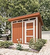 Petit cabanon ou dépendance en bois avec toit en pente et garniture blanche, entouré d'arbres verts luxuriants dans une cour arrière